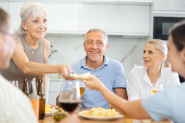 Fototapeta na wymiar Happy elderly people speaking to each other with enthusiasm while drinking and eating in the kitchen