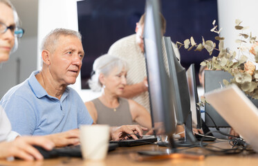 Concerned old man sitting at computer together with other attendees of IT courses