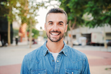 Close up portrait of handsome guy with perfect white teeth smiling and looking at camera standing outdoors. Front view of young man with friendly and positive expression. Happy adult male staring - Powered by Adobe