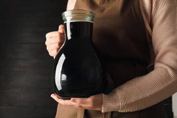 Woman with jug of tasty kvass on black wooden background - obrazy, fototapety, plakaty