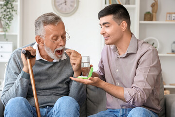 Senior man with his son taking pills at home - obrazy, fototapety, plakaty