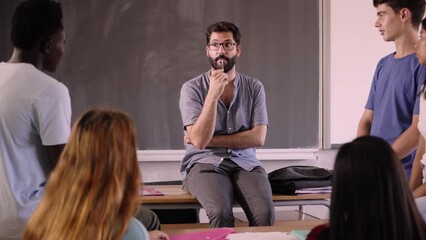 The teacher helps his students by answering their questions after class. Man sitting in informal attitude talking in meeting with his trainees. Generation z people learning new concepts.