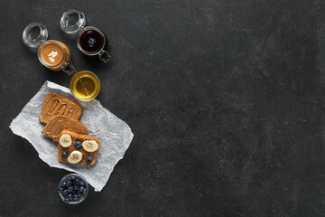 Baking paper of toasts with peanut butter, fresh fruits and honey on black background