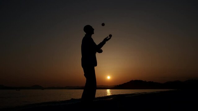 Silhouette of a man juggling at sunset. A man silhouette juggle with balls on the seashore againstcolorful orange sunset sky.