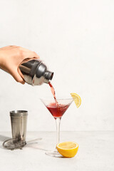 Woman pouring Cosmopolitan cocktail from shaker into glass on white background
