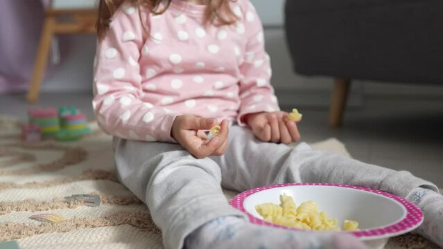 One girl caucasian toddler child eat macaroni pasta at home with hands