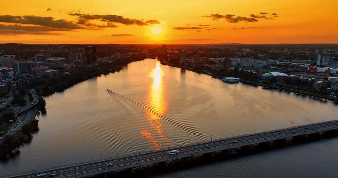 Single motor boat crossing the Charles River at sunset. Amazing scenery of Boston, Massachusetts, USA from top under orange sky.