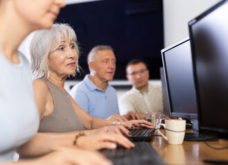 Elderly woman learns how to work with computer in group at computer course