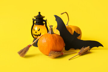 Halloween composition with pumpkins, brooms, bat and lantern on yellow background