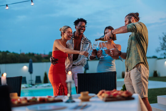 Guy is pouring champagne for his friends at a poolside dinner party