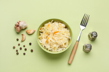 Bowl of tasty sauerkraut with spices and garlic on green background