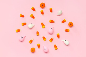 Halloween composition with ghosts, candy corns and pumpkins on pink background