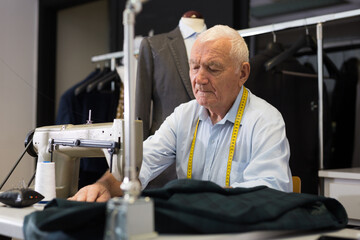 Portrait of elderly man tailor working on sewing machine at studio