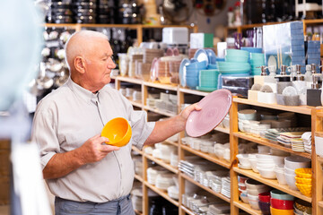 Elderly man looking for new tableware at store of household goods