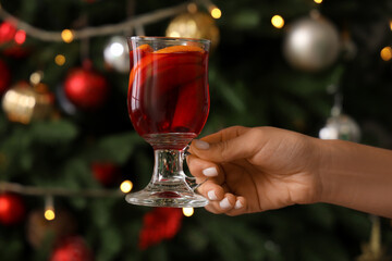Young woman with glass of mulled wine at home on Christmas eve, closeup