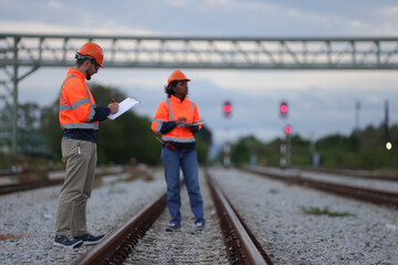 A couple of Railway engineers with orange safety jackets checking the railway at  the train station