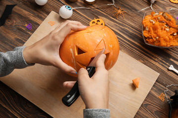 Woman carving Halloween pumpkin at wooden table