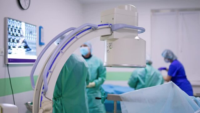 C-Arm x-ray machine standing over the patient in surgery room. Surgeon study x-ray scans near the screen.