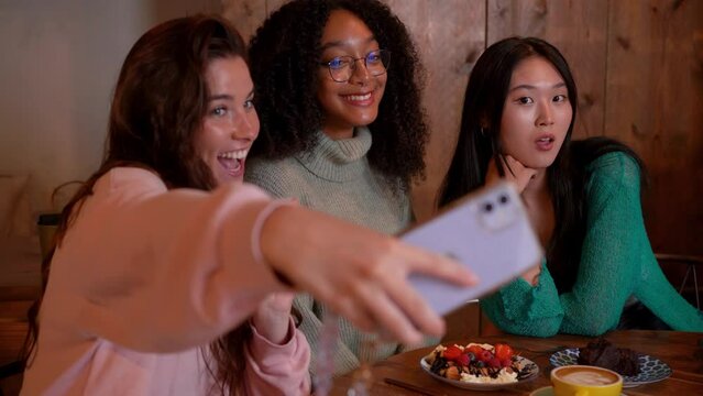 A group of smiling young women taking a selfie photo with a smart phone. They are having a brunch.