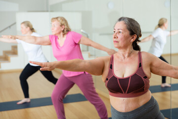 Mature women making yoga at gym. Virabhadrasana pose