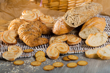 Fototapeta na wymiar Freshly baked wheat and grain baguettes, croissants and different biscuits on wicker background