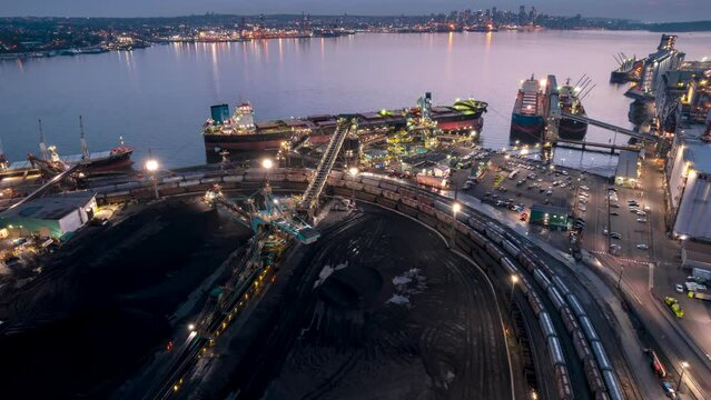 Rotary shovel at coal pile loading freight vessels at bulk shipping terminal, aerial hyperlapse, silos, grain elevators, freight vessels, North Vancouver, BC. 4K 24FPS