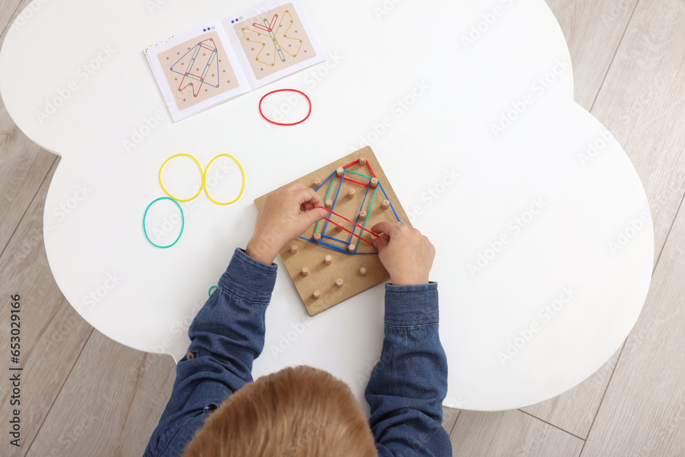 Poster Motor skills development. Boy playing with geoboard and rubber bands at white table, top view