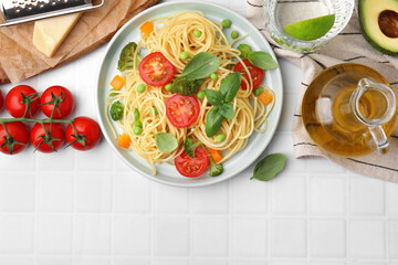 Plate of delicious pasta primavera and ingredients on white tiled table, flat lay
