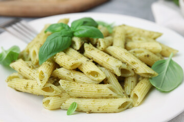 Delicious pasta with pesto sauce and basil on plate, closeup