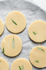 Top view of cut out raw rosemary sugar cookie dough, rosemary cookie dough about to be baked, process of making rosemary sugar cookies