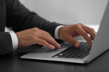 Man using modern laptop at black desk, closeup