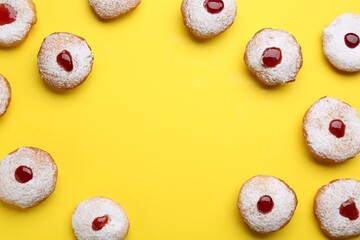 Frame of Hanukkah donuts with jelly and powdered sugar on yellow background, flat lay. Space for...