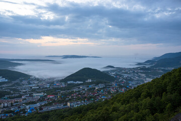 Morning misty landscape. Top view of the city and surroundings. Fog and low clouds over the city and hills. Residential urban areas at dawn. Petropavlovsk-Kamchatsky, Kamchatka, Far East of Russia.