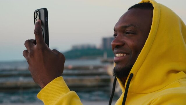 African American man takes pictures on mobile phone near sea
