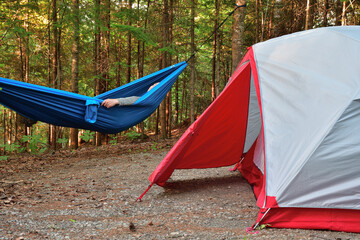 Happy camper relaxing. Camping setup with gray and red tent and bleu hammock