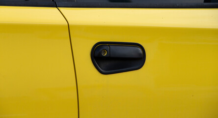 Yellow car door handle with keyhole on the side of a yellow car