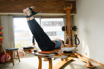 Caucasian woman lying on back on exercise machine with pulleys and weights, legs extended upwards