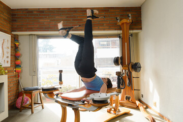 Caucasian woman lying on back on exercise machine with pulleys and weights, legs extended upwards - obrazy, fototapety, plakaty