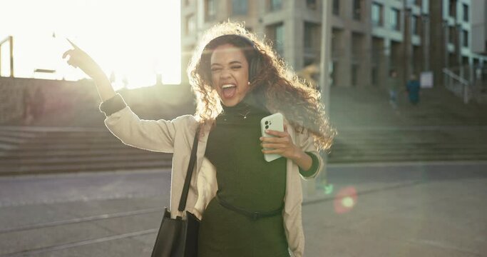 Woman, happy and dancing to music in city morning with sunshine, happiness and celebration of freedom. Listening, dance and streaming techno or hip hop audio or person with crazy or funny expression