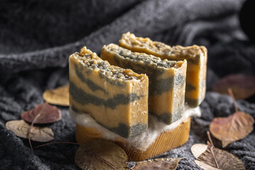 Pieces of handmade natural soap on a wooden soap dish against the background of a warm sweater and dry leaves. Concept of a cozy autumn atmosphere, organic cosmetics for the skin care