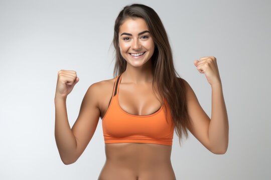Portrait of a smiling sportswoman in orange sportswear showing her biceps isolated on a white background and Looking at the camera.