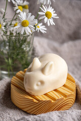 Natural handmade soap in the shape of cute rabbits on a wooden soap dish on a background of chamomile flowers. Concept of using eco friendly products for the care of delicate baby skin