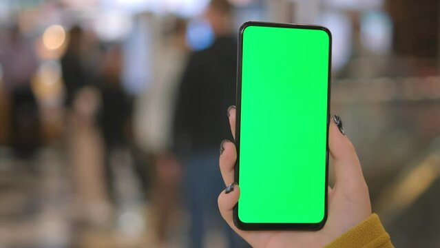 Mall. Use green screen for copy space closeup. Chroma key mock-up on smartphone in hand. Woman holds mobile phone and looking photos or pictures