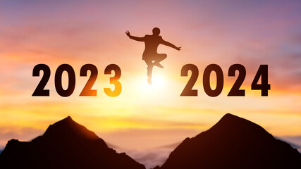 Silhouette of a person leaping from 2023 to 2024 on the top of the mountain background. Happy New Year and Christmas day concept.