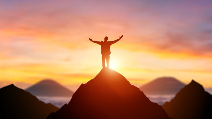 Silhouette of a business person on the top of a mountain peak in sunset background. Winner and...