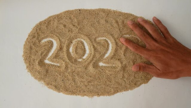 A hand removes the number 3 replacing it with the number 4 on the sand, change of year 2023 to 2024. Concept of change of new year 2023 to 2024