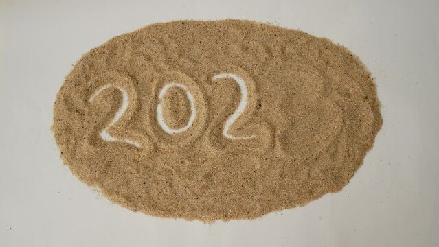 A hand removes the number 3 replacing it with the number 4 on the sand, change of year 2023 to 2024. Concept of change of new year 2023 to 2024
