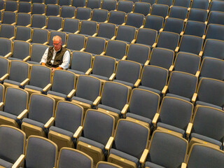 Naklejka premium Overhead view a middle age man with gray hair sitting alone in an empty, auditorium seats, chairs.