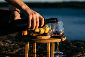 Male hands pour red wine into a glass on a background of nature