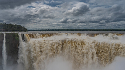 The famous Devil's throat waterfall. Stormy streams plunge into the abyss. The water is bubbling, foaming. Splashes all around. Clouds in the blue sky. Iguazu Falls. Argentina.
